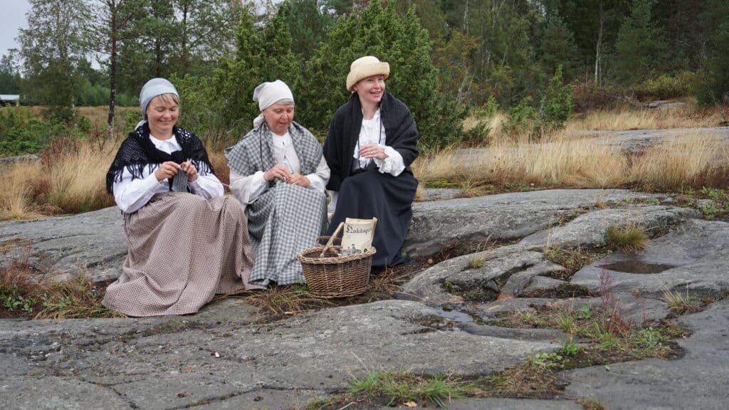 Naiset istuvat Davidsbergin kalliolla ja juttelevat. Kuva on otettu virtuaaliopasteiden kuvauksissa. Kuvan näyttelijät ovat Kokkolan matkailuoppaita.