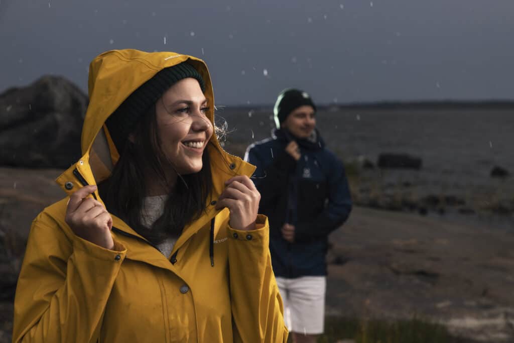 A woman and a man in the rain, dark clouds in the background. A woman in a yellow raincoat is smiling.