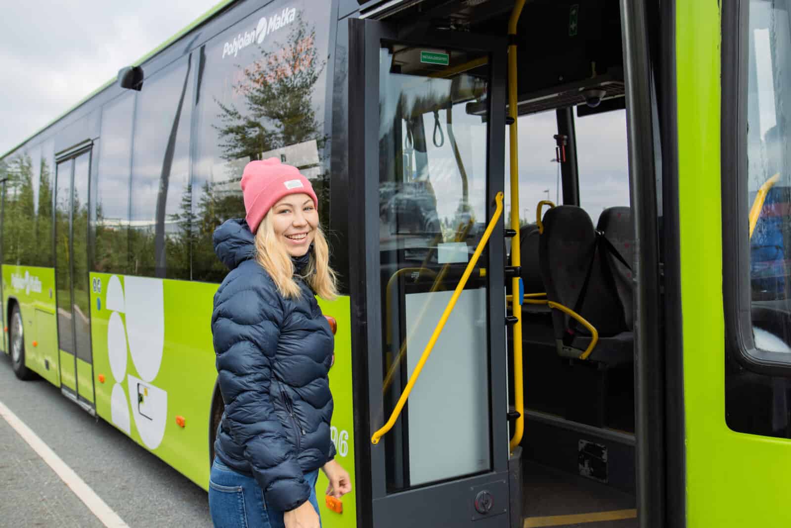 Nainen hymyilee bussin edessä