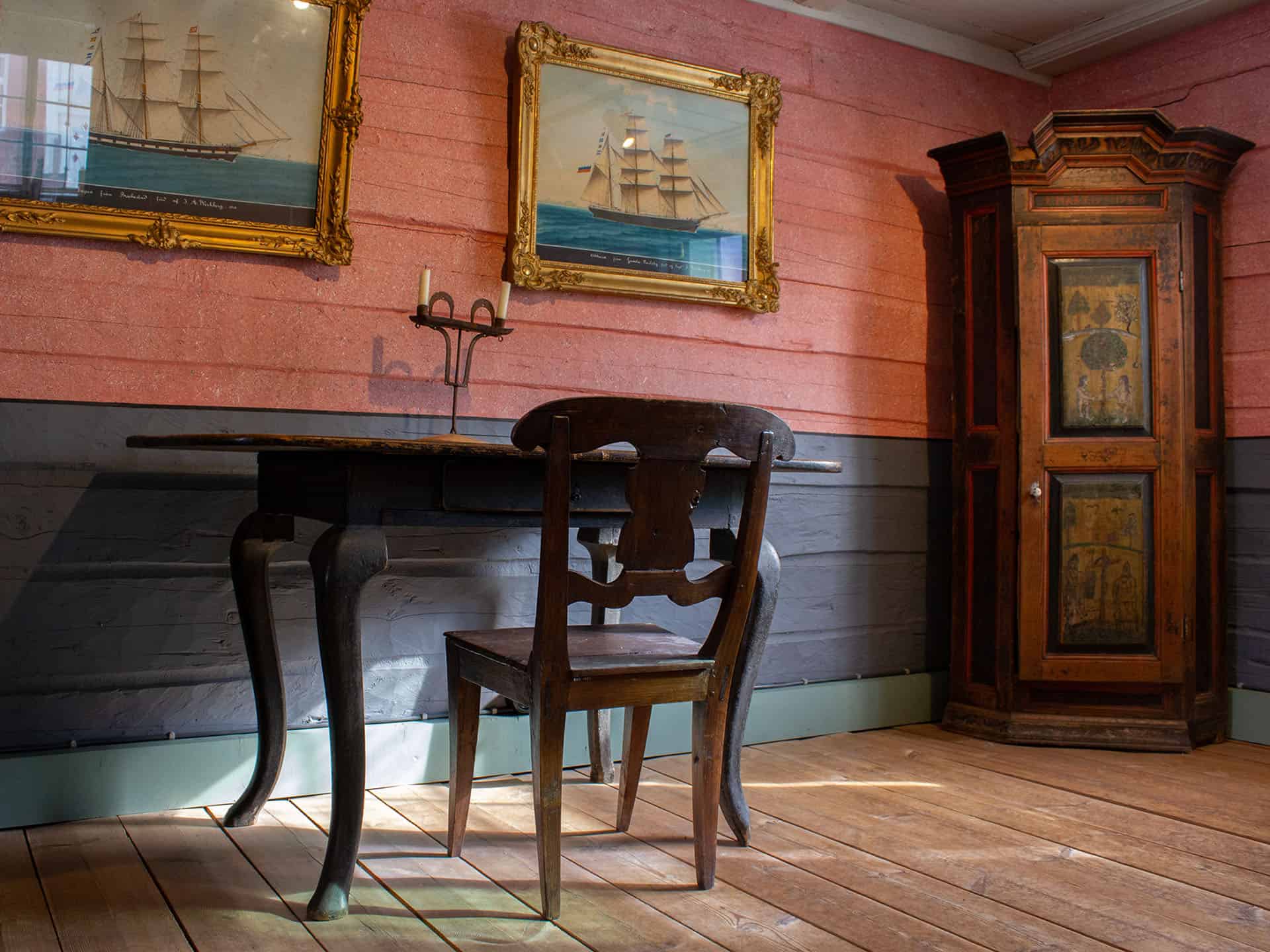 Lassanderin talon sisältä otettu kuva, jossa vanha kirjoituspöytä ja tuoli sekä koristeellinen kaappi. Seinällä kaksi taulua laivoista.
