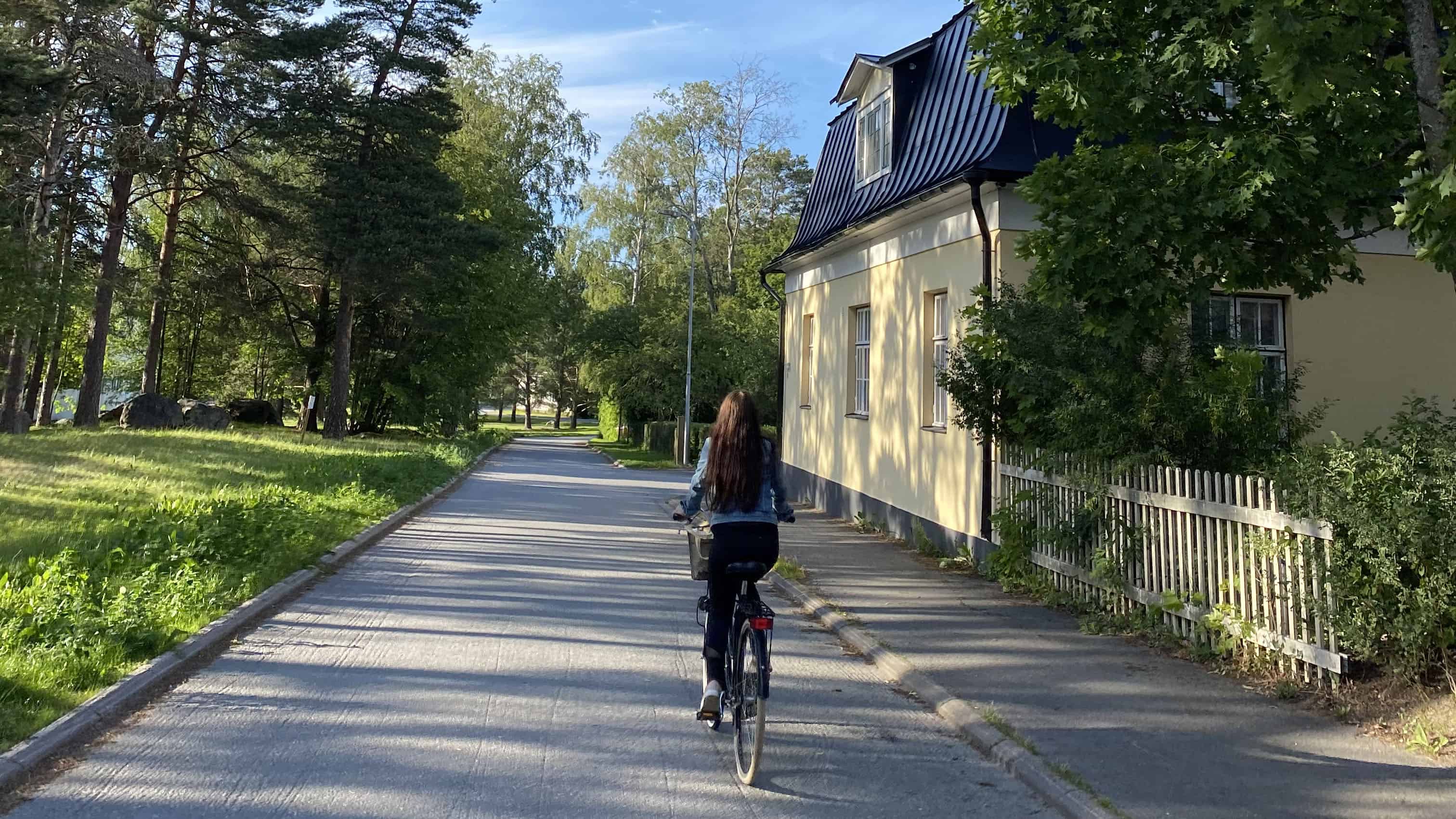 Nainen ajaa pyörällä Mäntykankaan alueen kadulla. Sää on aurinkoisen kesäinen.