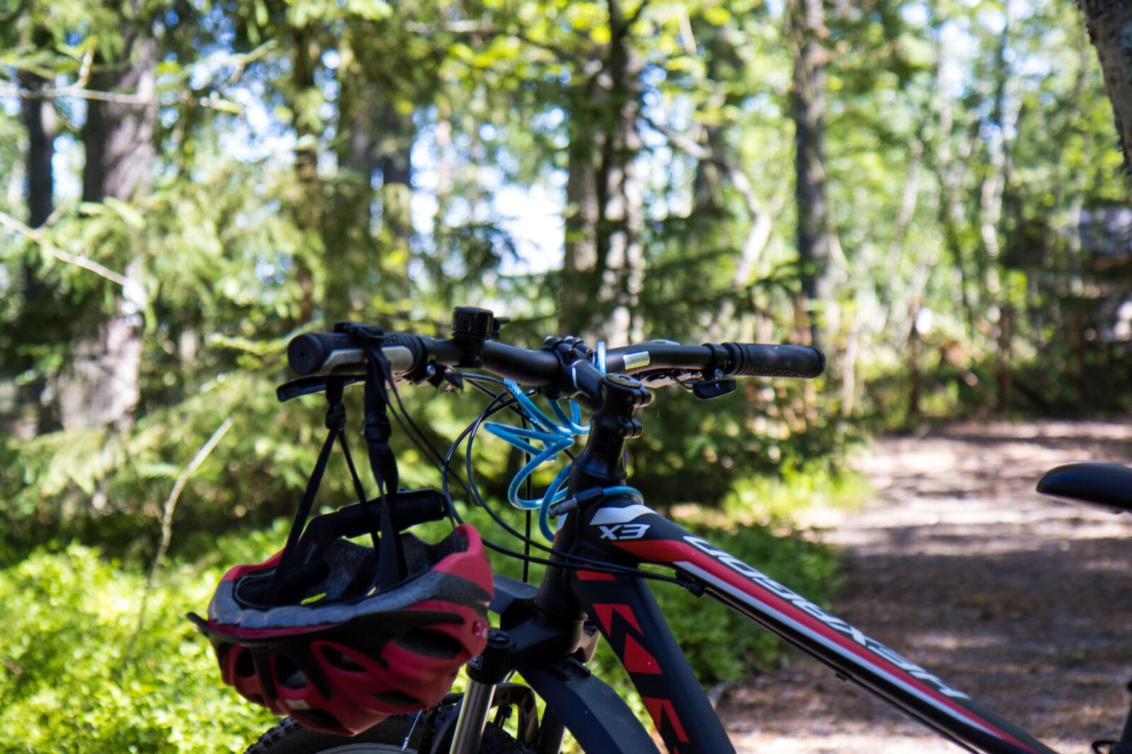 Polkupyörä pysäköitynä metsäreitille, pyörän ohjaustangosta roikkuu kypärä. Taustalla vihreää keväistä metsää.