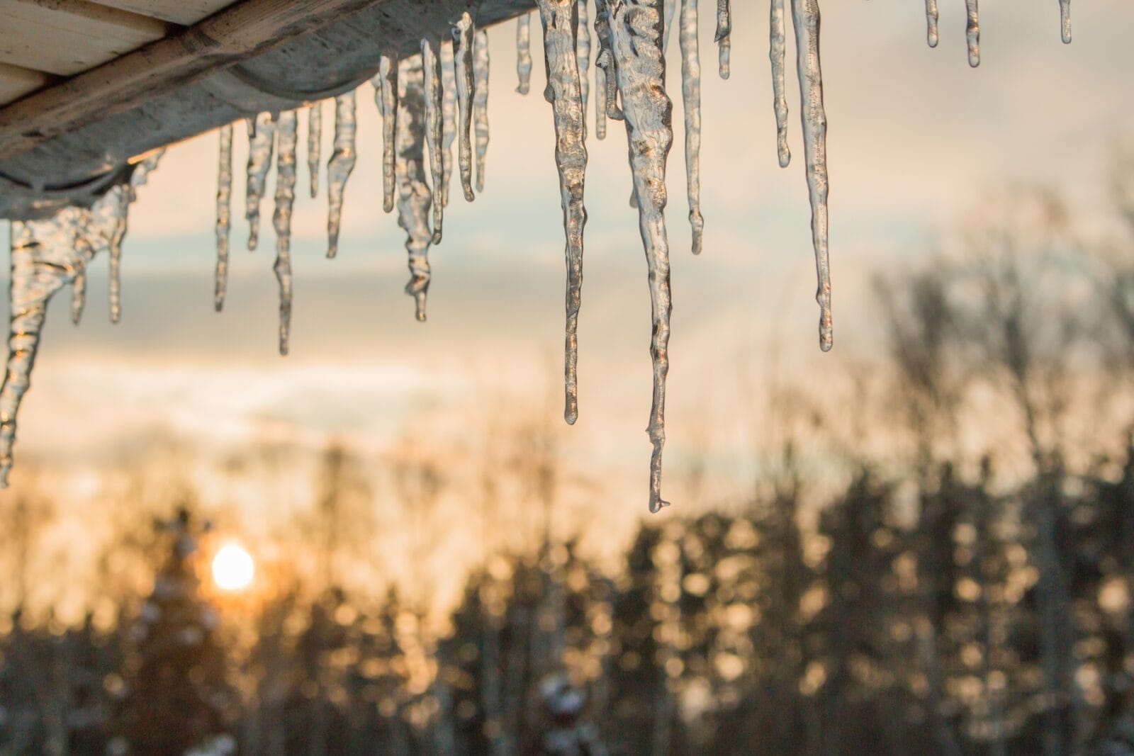 Jääpuikkoja räystäällä, taustalla näkyy talvinen auringonnousu